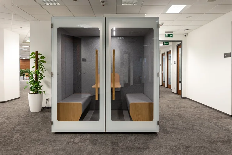 Two large HIDE H4 acoustic booths in a bright open-space corridor with benches and a plant