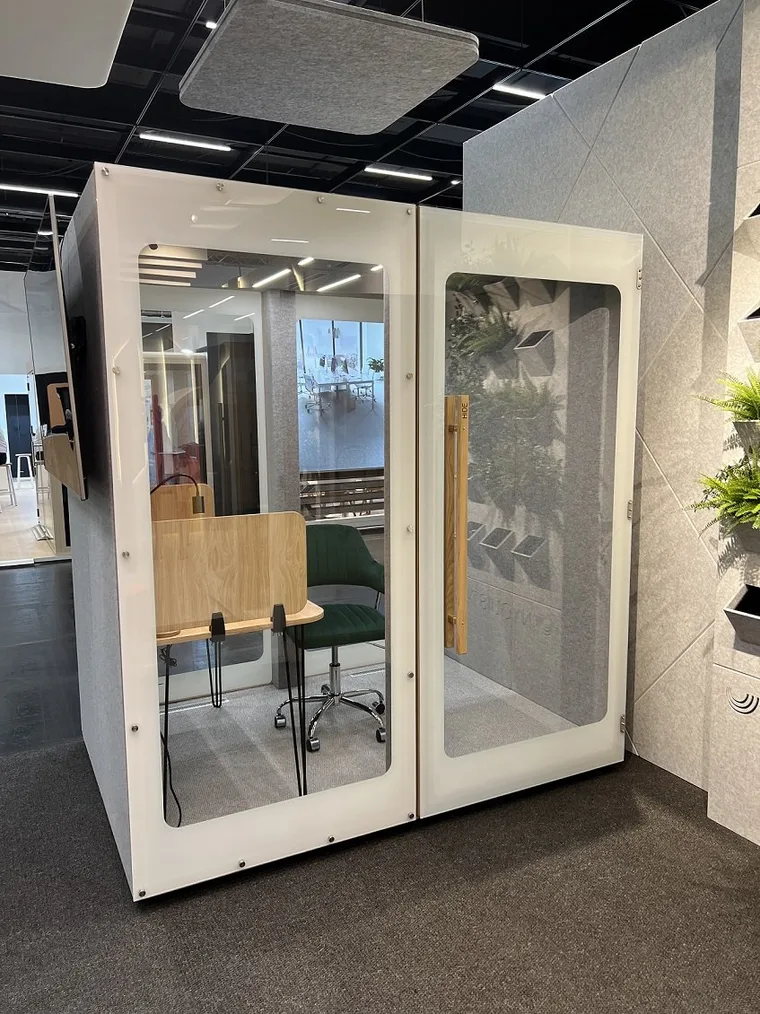 Cabine HIDE Mini Office avec bureau et fauteuil vert près d'un mur végétal décoratif
