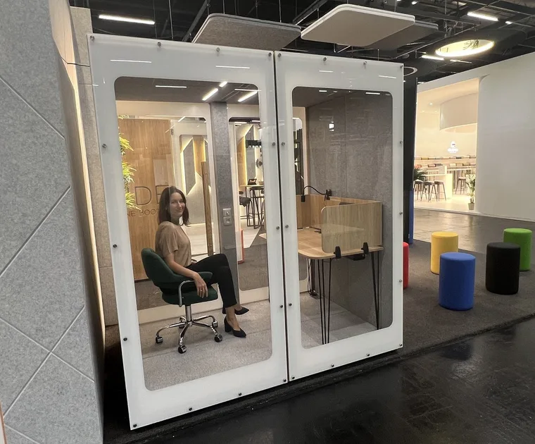 Cabine HIDE Mini Office sur un stand de salon, une femme assise au bureau à l'intérieur
