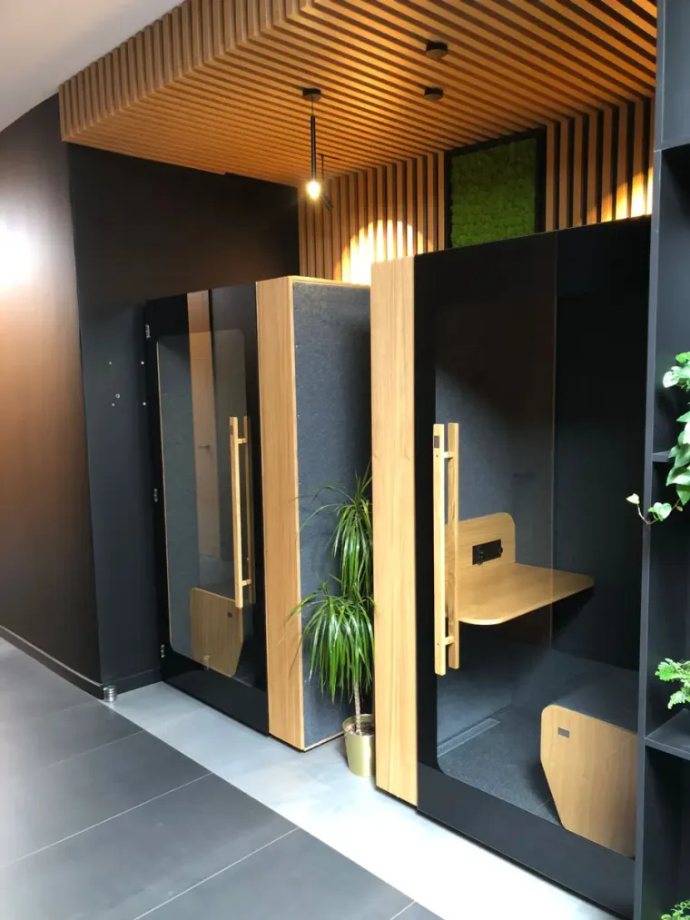Two dark HIDE H1+ acoustic booths in a reception area with a wood-slat ceiling and moss wall