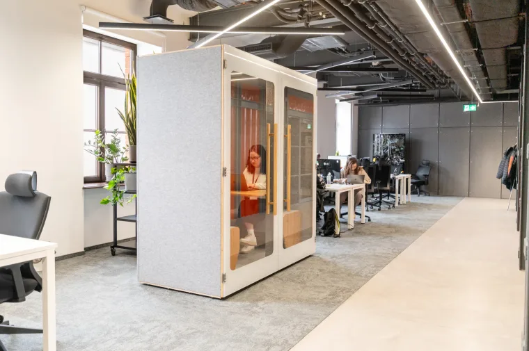 HIDE H2 acoustic booth in an open-plan office with exposed ceiling, a woman working on a laptop inside