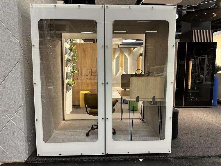 Cabine HIDE Mini Office sur un stand de salon avec mur en bois, plantes et fauteuil de bureau doré