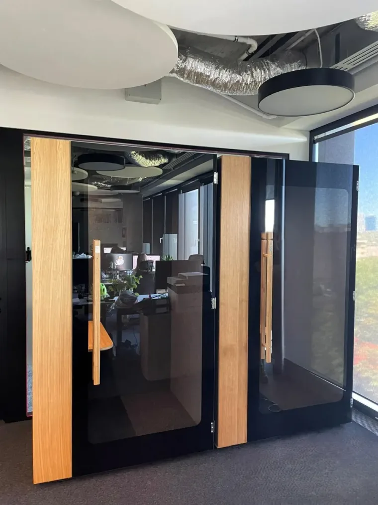 Two dark HIDE H1+ acoustic booths by a large window with a city view
