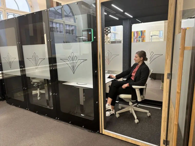 Une rangée de cabines HIDE Mini Office sombres au verre décoratif gravé, une femme travaille dans un intérieur historique