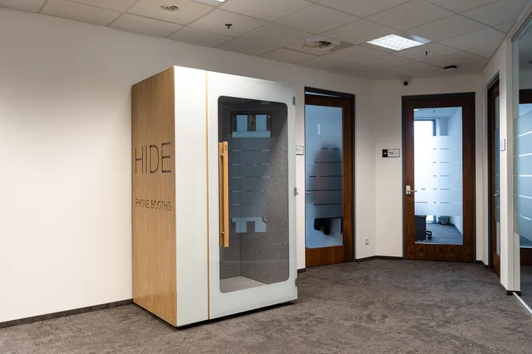 HIDE H1+ acoustic booth with a wood panel and logo in an office corridor with meeting room doors