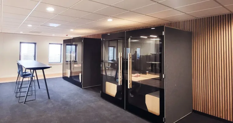 Two black HIDE H4 acoustic booths by a wood-slat wall, with a tall table nearby