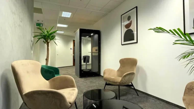 A black HIDE H1 acoustic booth in an elegant waiting area with beige armchairs and plants