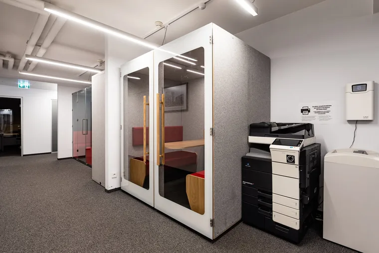 HIDE H4 acoustic booth with red bench seating in a corridor next to an office printer