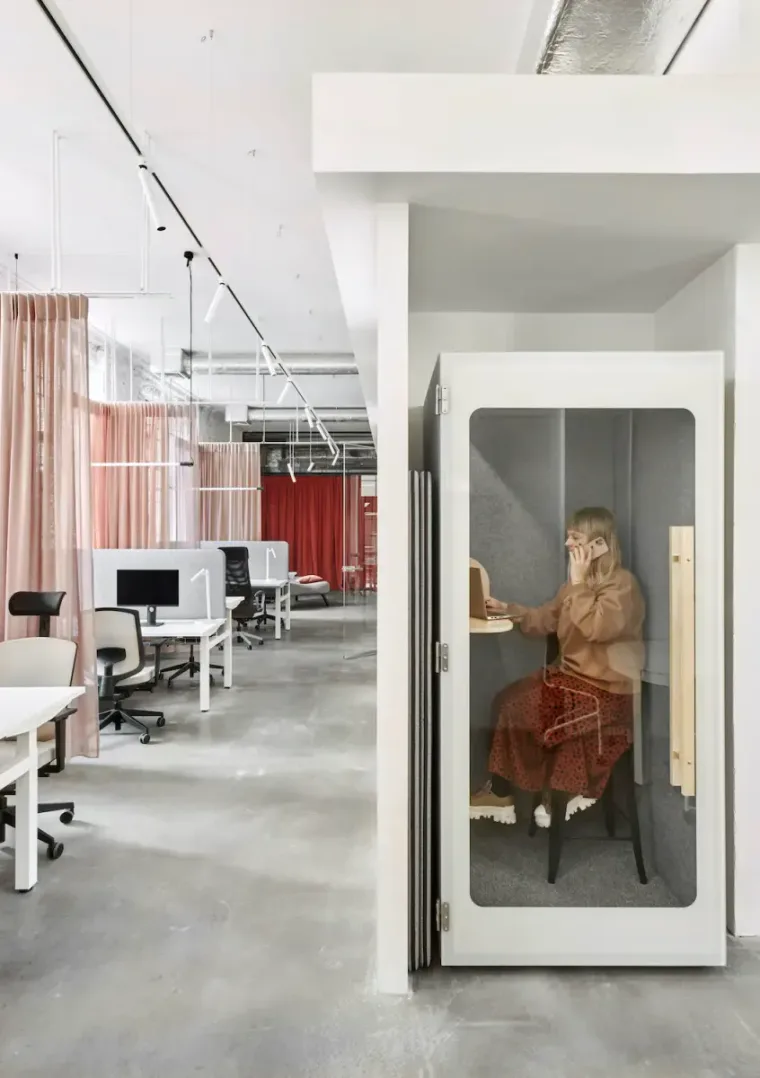 A woman works on a laptop and talks on the phone inside a light HIDE H1 acoustic booth