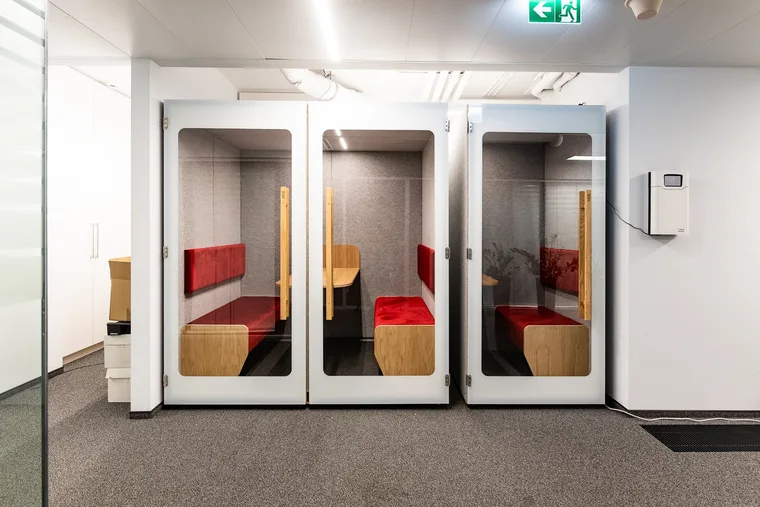 Two white HIDE H1 acoustic booths with red bench seating standing side by side in a corridor